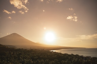 The sun is setting over a mountain with a body of water in the foreground