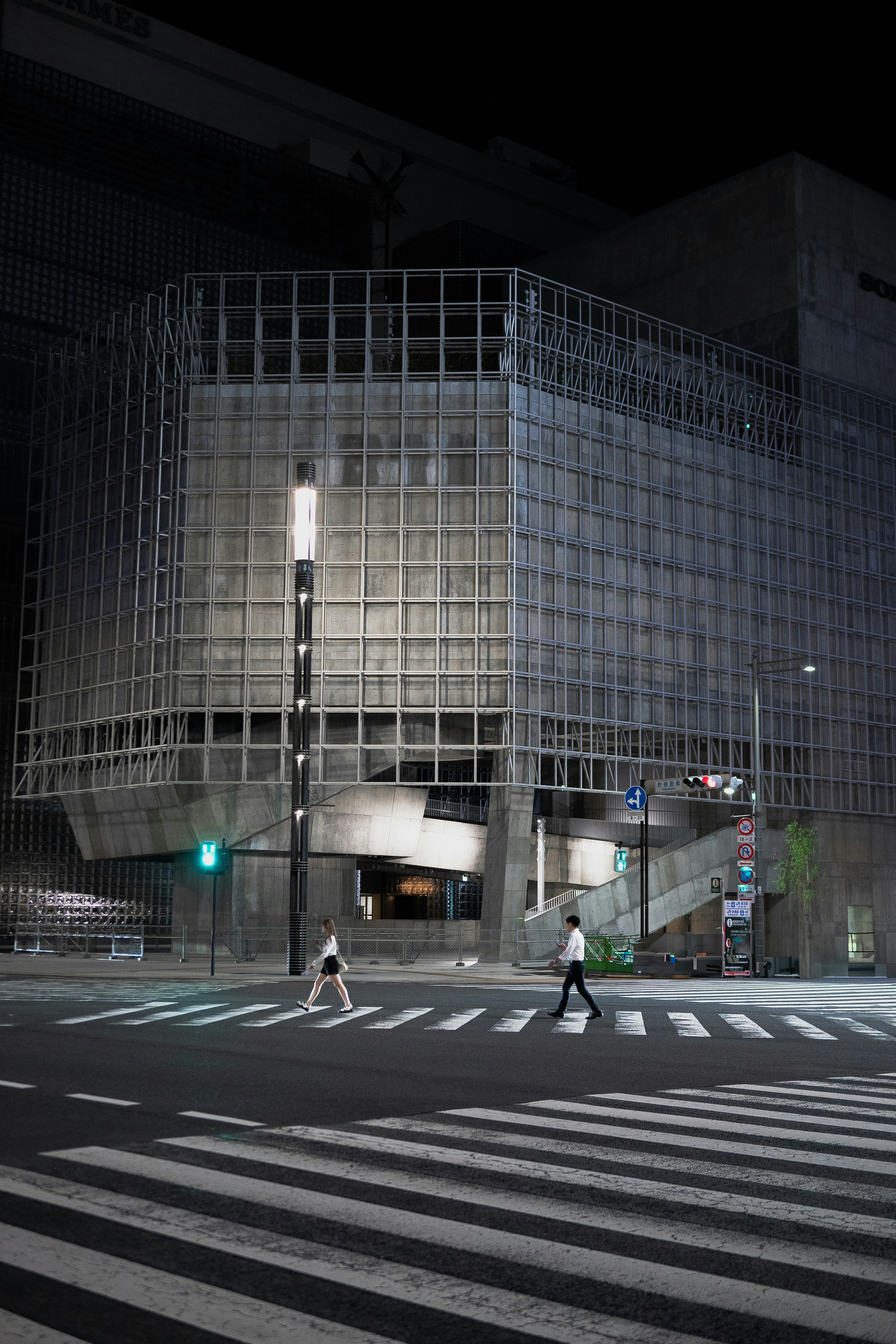 A person crossing a street at night in front of a building