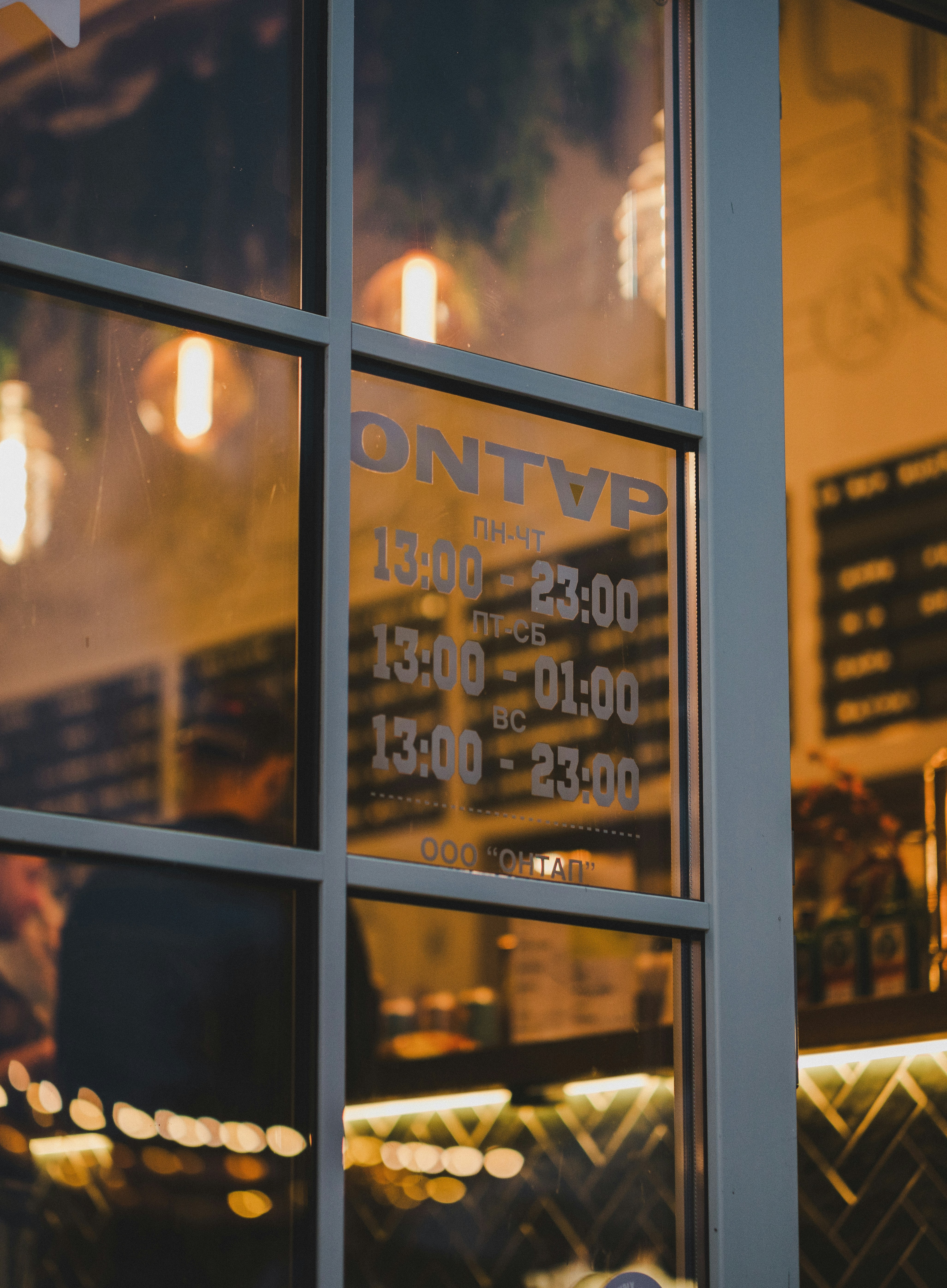 Storefront glass with vinyl business name lettering and hours, warm interior lighting