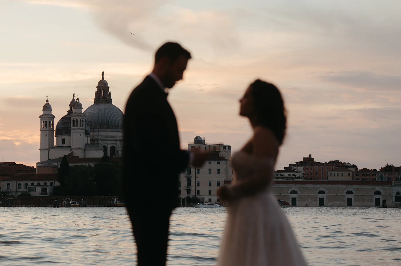 Couple in elopement attire on the Ile d’Orleans riverfront with the Quebec City skyline and the Chateau Frontenac visible across the St. Lawrence River in the afternoon light