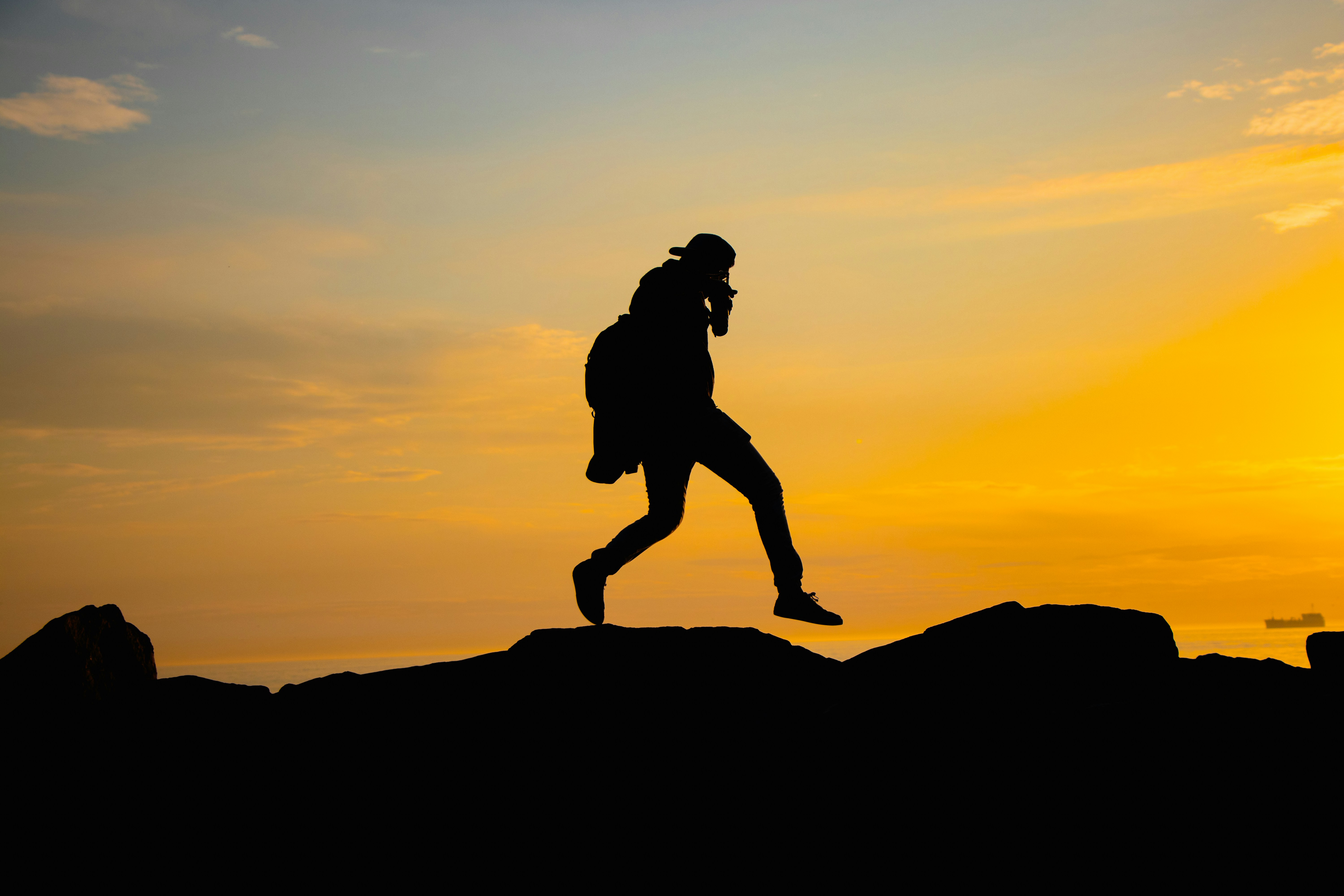 A silhouette of a man running on a hill at sunset