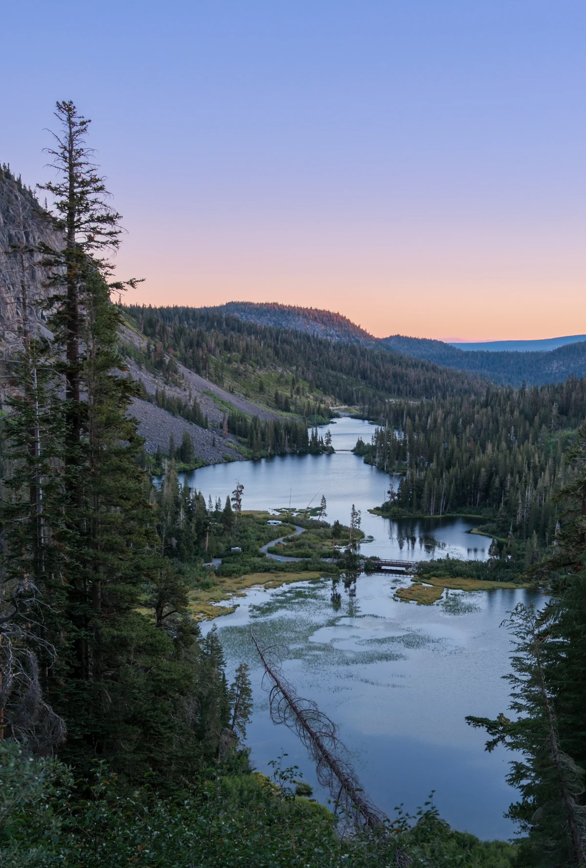 Twin Lakes seen from the overlook above them, the forest running down to the water under a pink sky