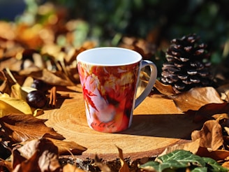 A fall-themed coffee cup sitting on top of a pile of leaves