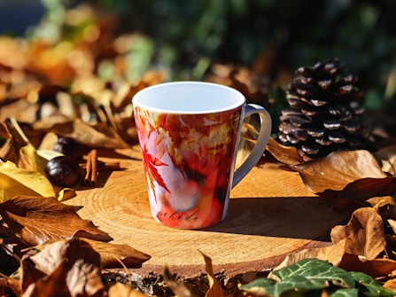 A fall-themed coffee cup sitting on top of a pile of leaves