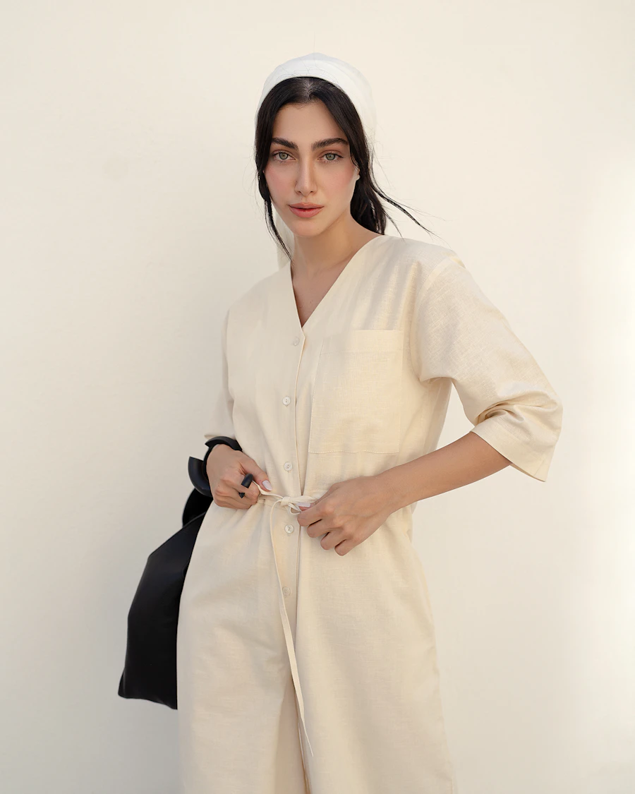 Woman in a cream buttoned linen shirt dress holding a black bag