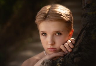 A woman leaning against a tree with her hand on her face