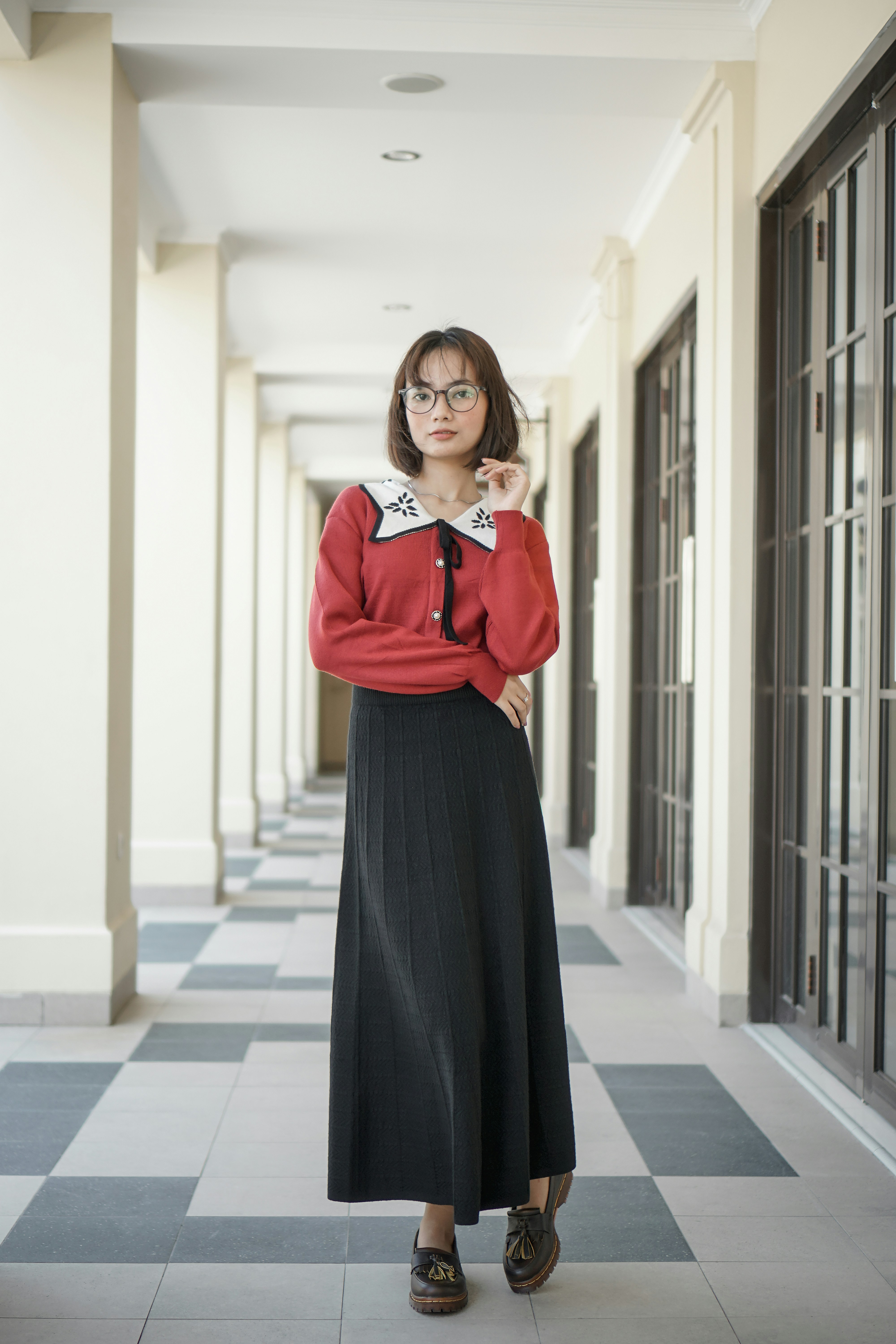 A woman standing in a hallway with a red shirt and black skirt