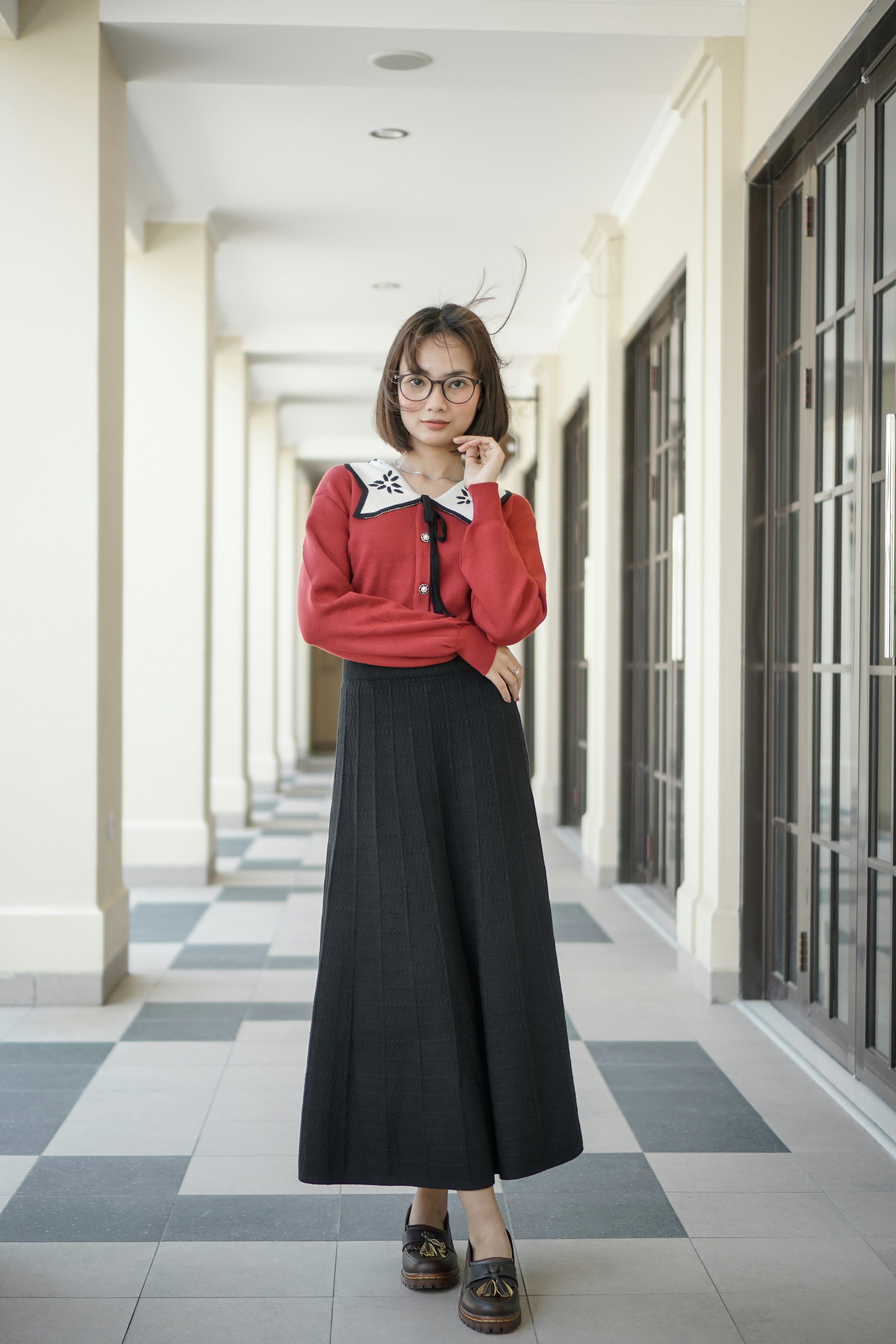 A woman standing in a hallway wearing a red shirt and black skirt