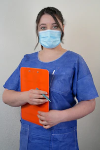 A woman wearing a surgical mask holding a clipboard