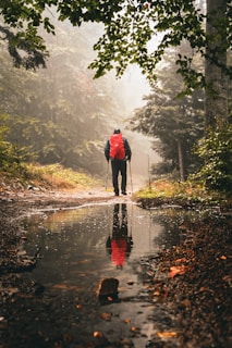 A man with a red backpack is walking in the rain