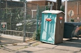 A trash can sitting on the side of a road next to a fence