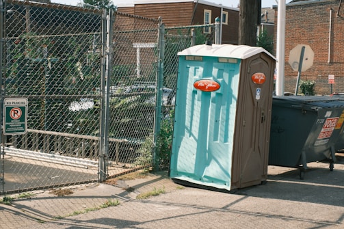 A trash can sitting on the side of a road next to a fence