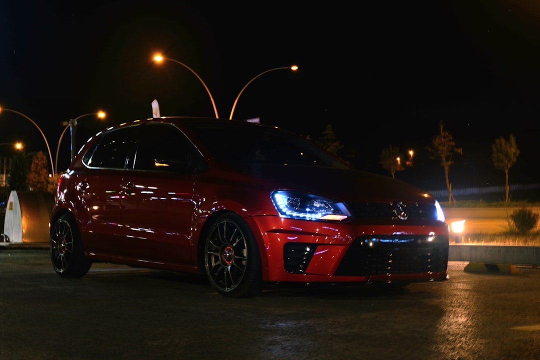 A red car parked in a parking lot at night,
