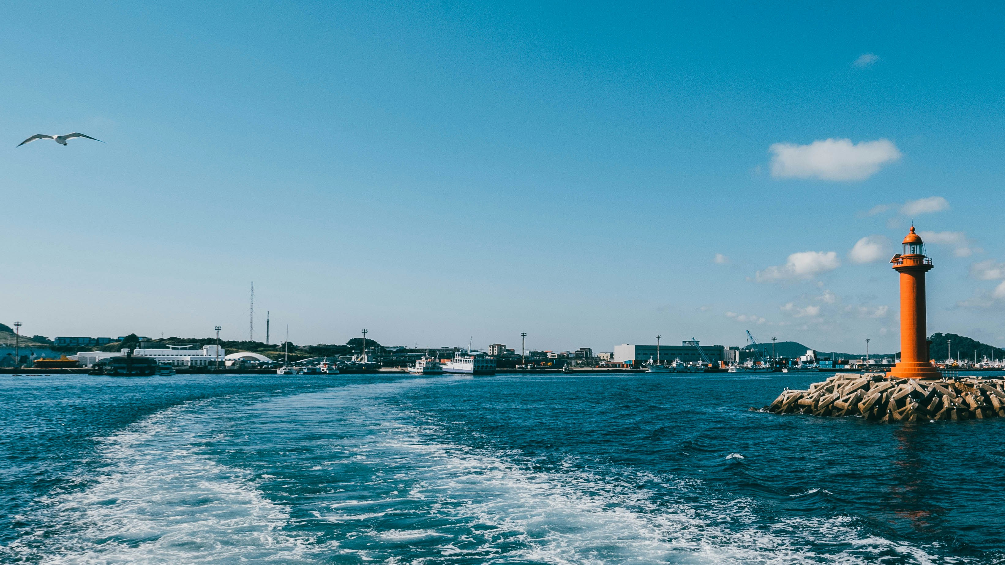A boat traveling down a body of water near a light house