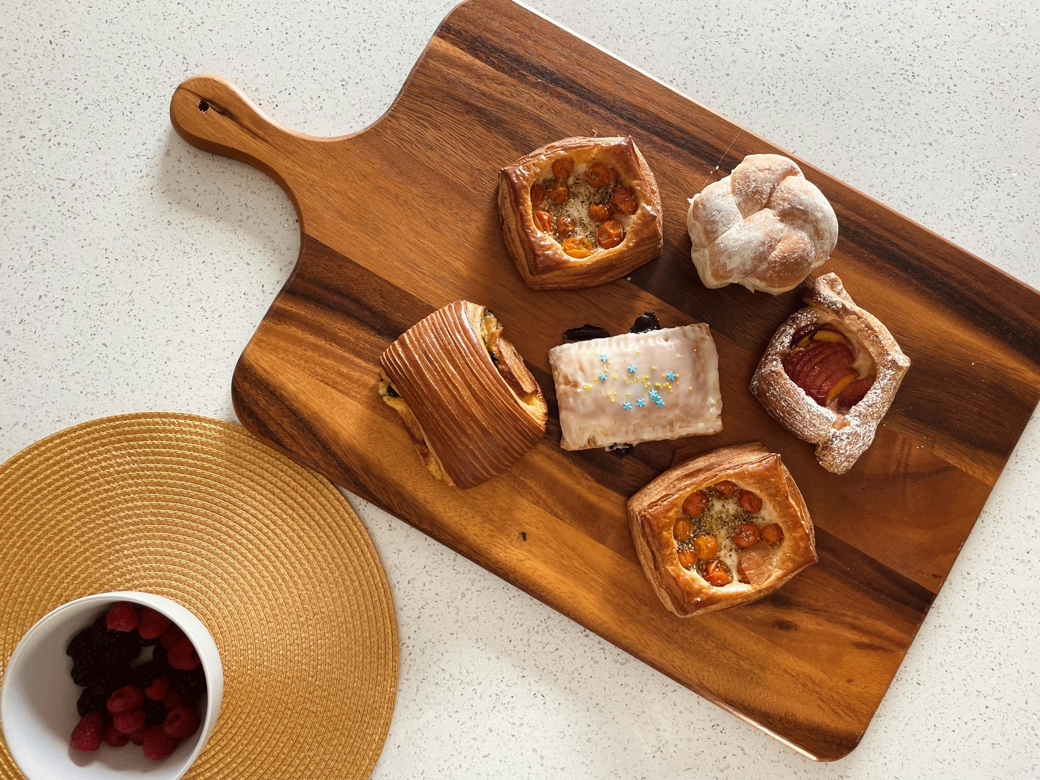 A wooden cutting board topped with pastries next to a cup of coffee