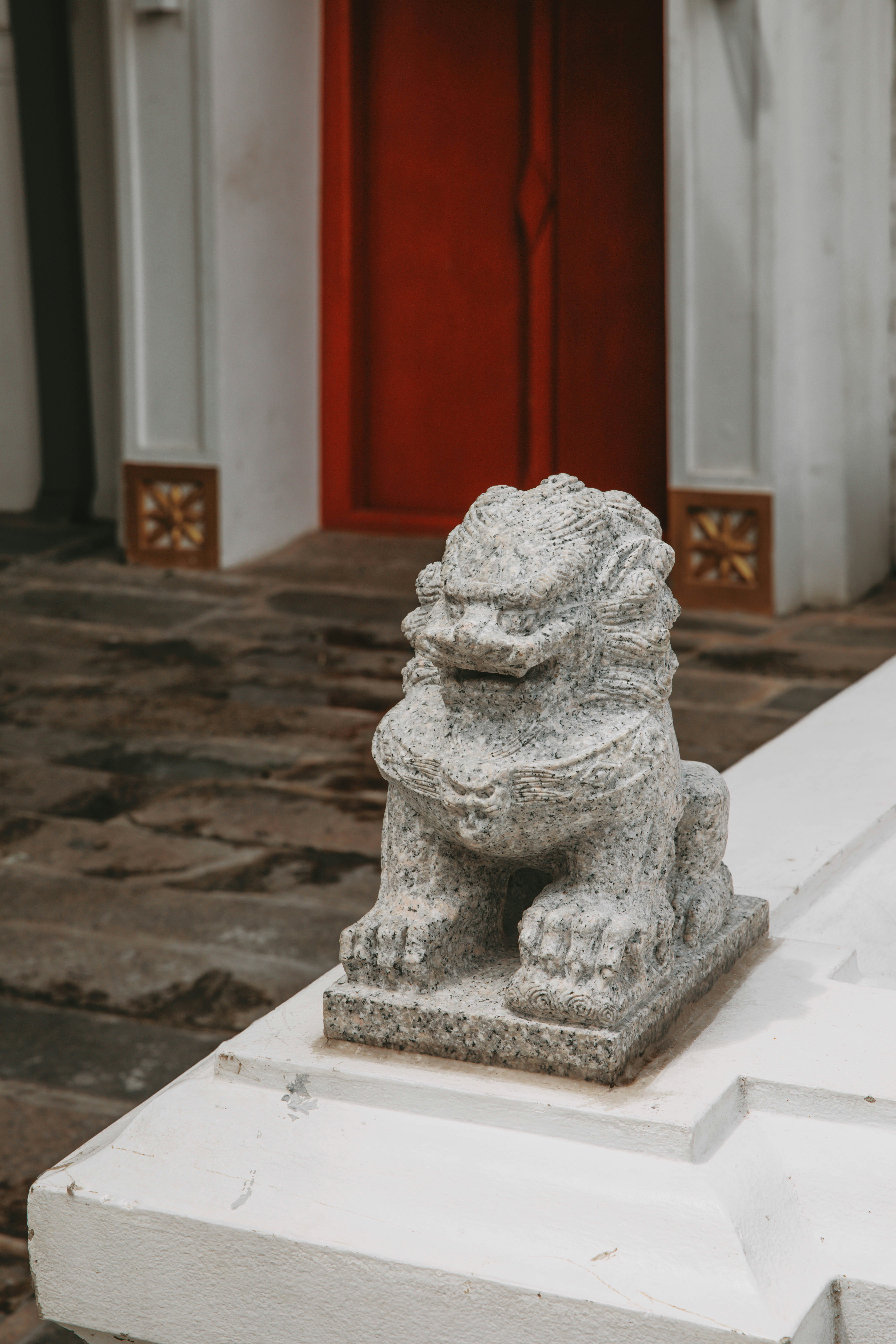 A statue of a lion on a pedestal in front of a red door