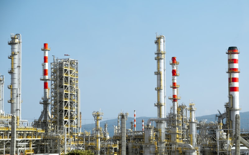 An oil refinery with red and white industrial pipes and chimneys