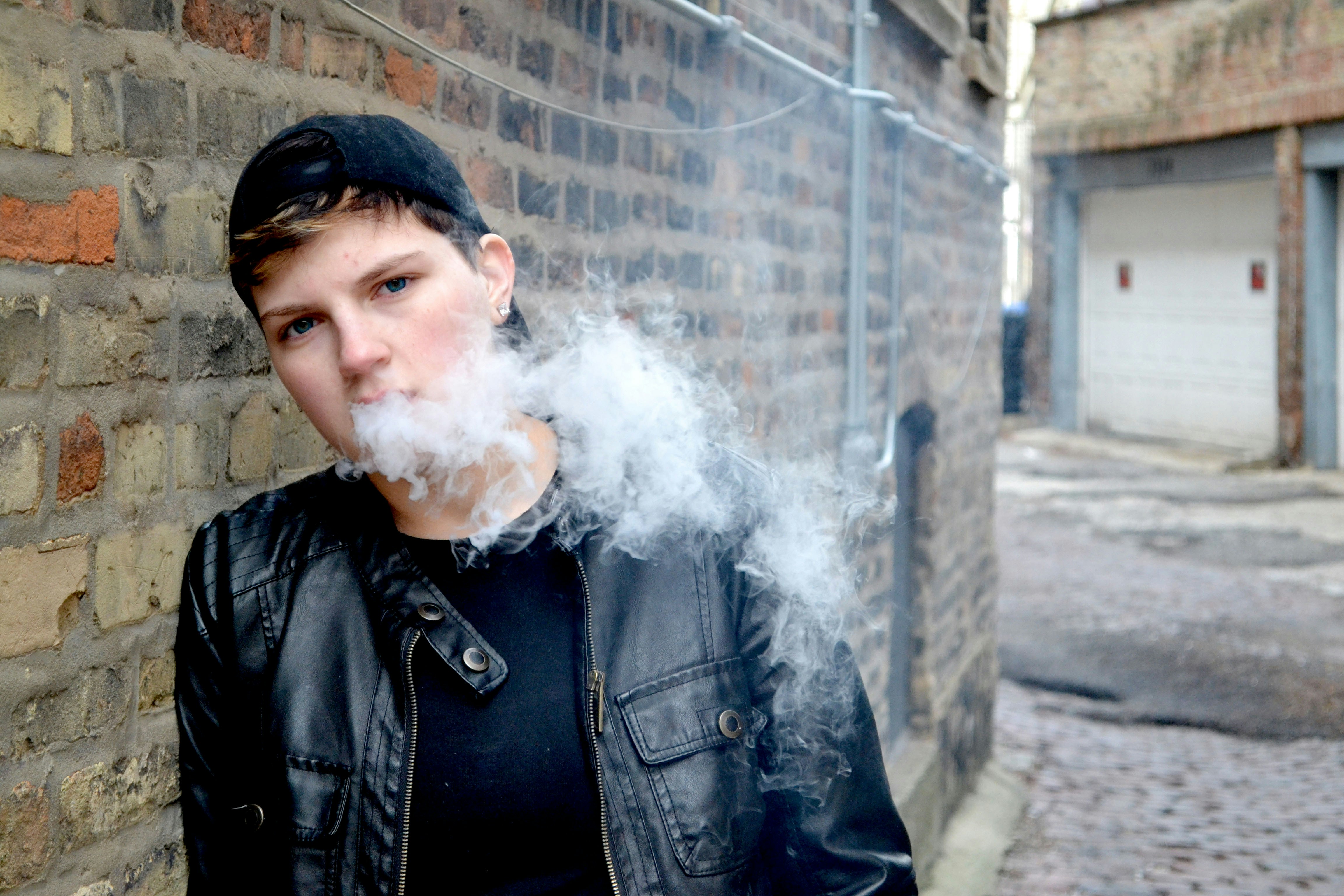 A man smoking a cigarette in front of a brick wall photo – Free Man Image  on Unsplash