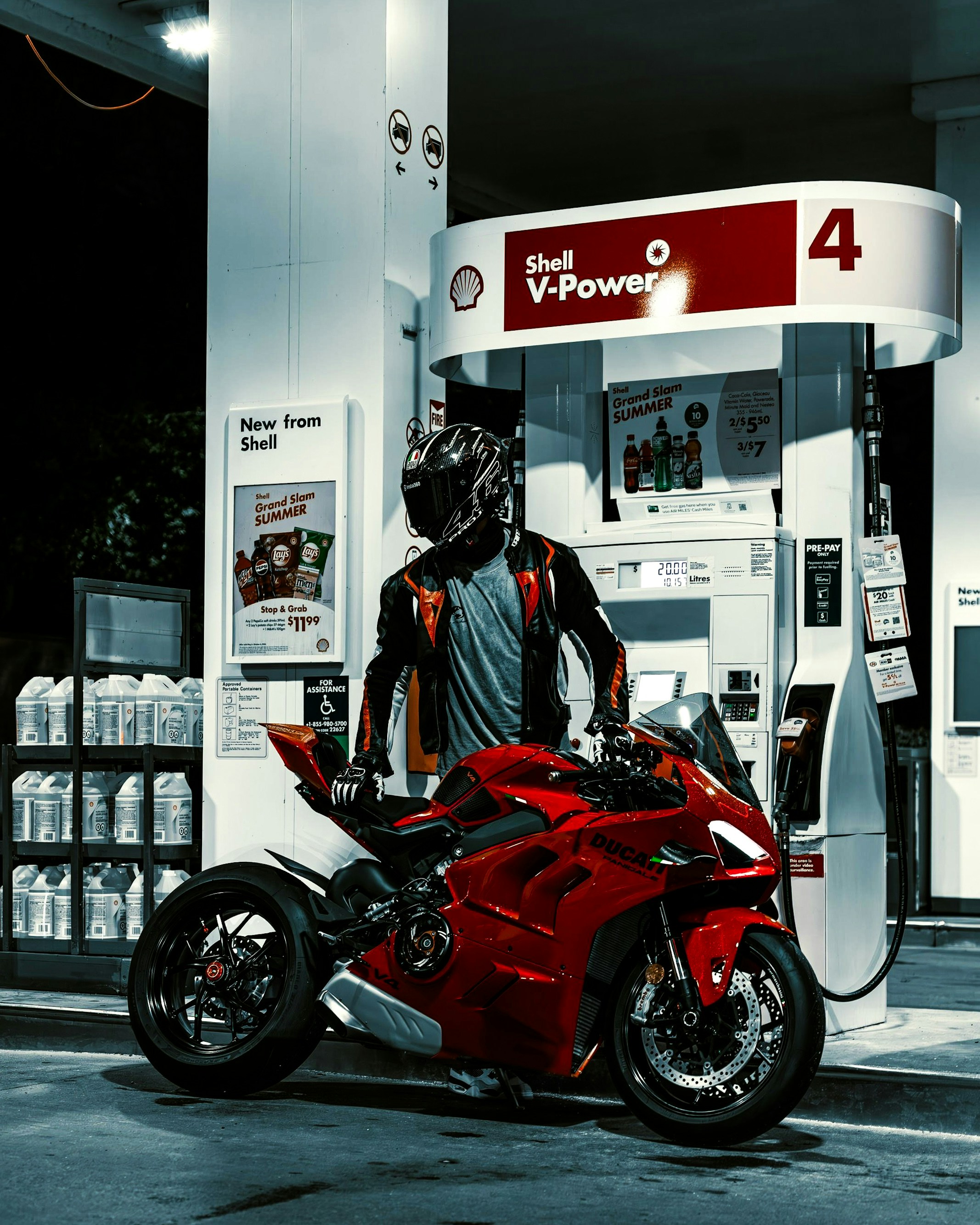 A man standing next to a red motorcycle at a gas station