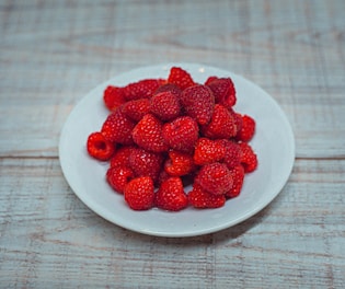 A white plate of strawberries on a wooden table