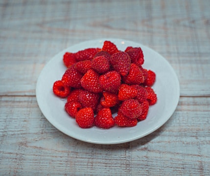 A white plate of strawberries on a wooden table