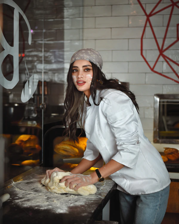 A baker in a white shirt shaping fresh bread dough in her bakery