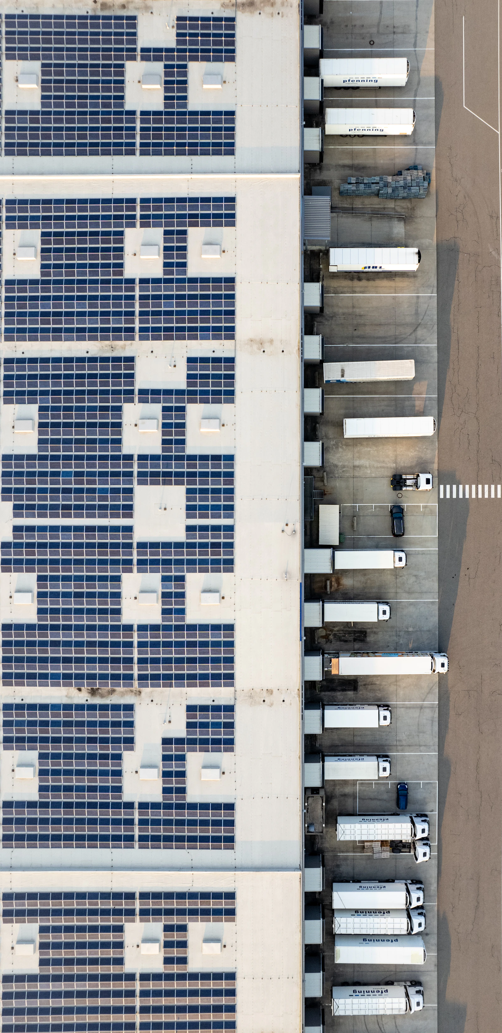 An aerial view of a large flat industrial roof with solar panels
