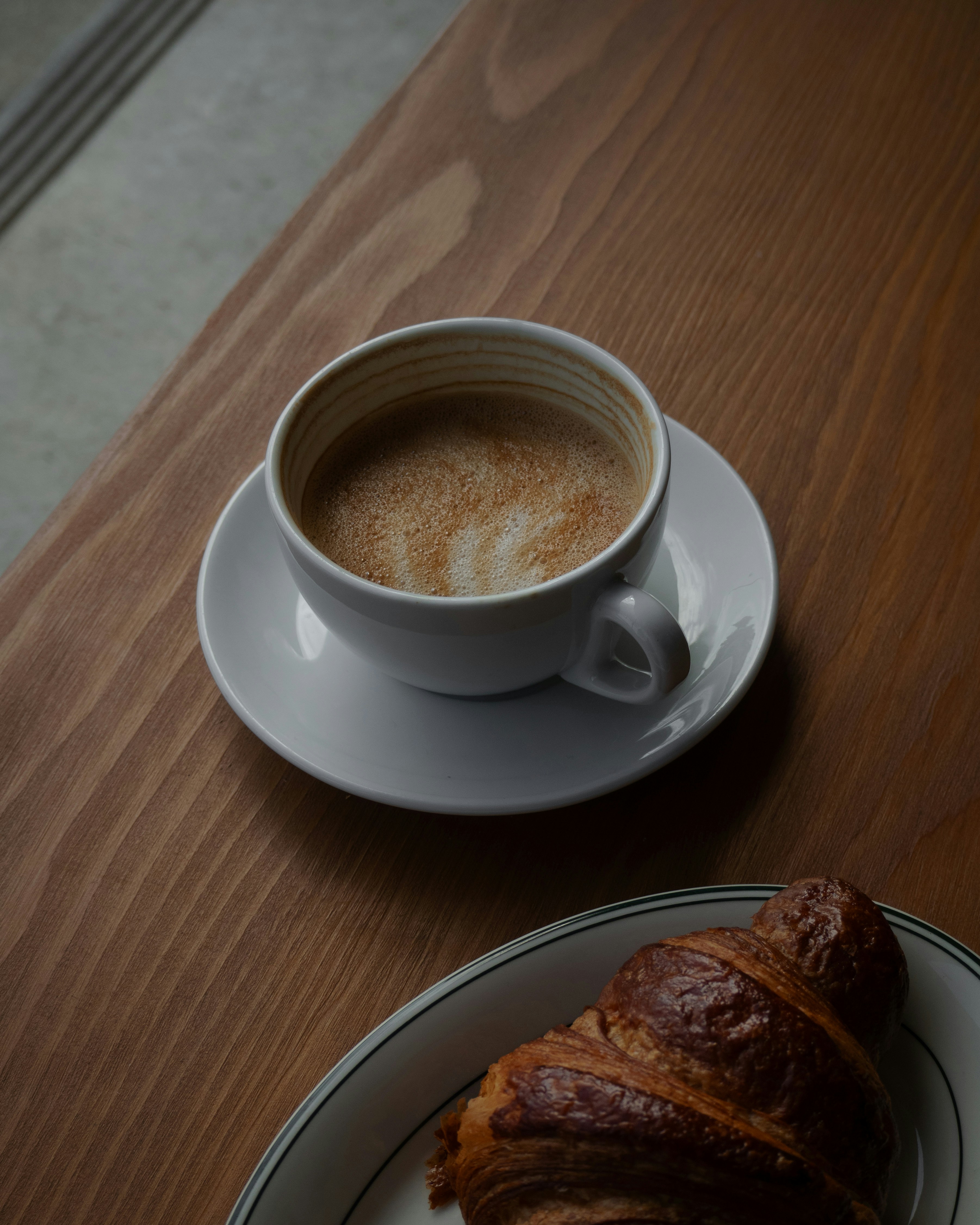 Ein Croissant auf einem Teller neben einer Tasse Kaffee