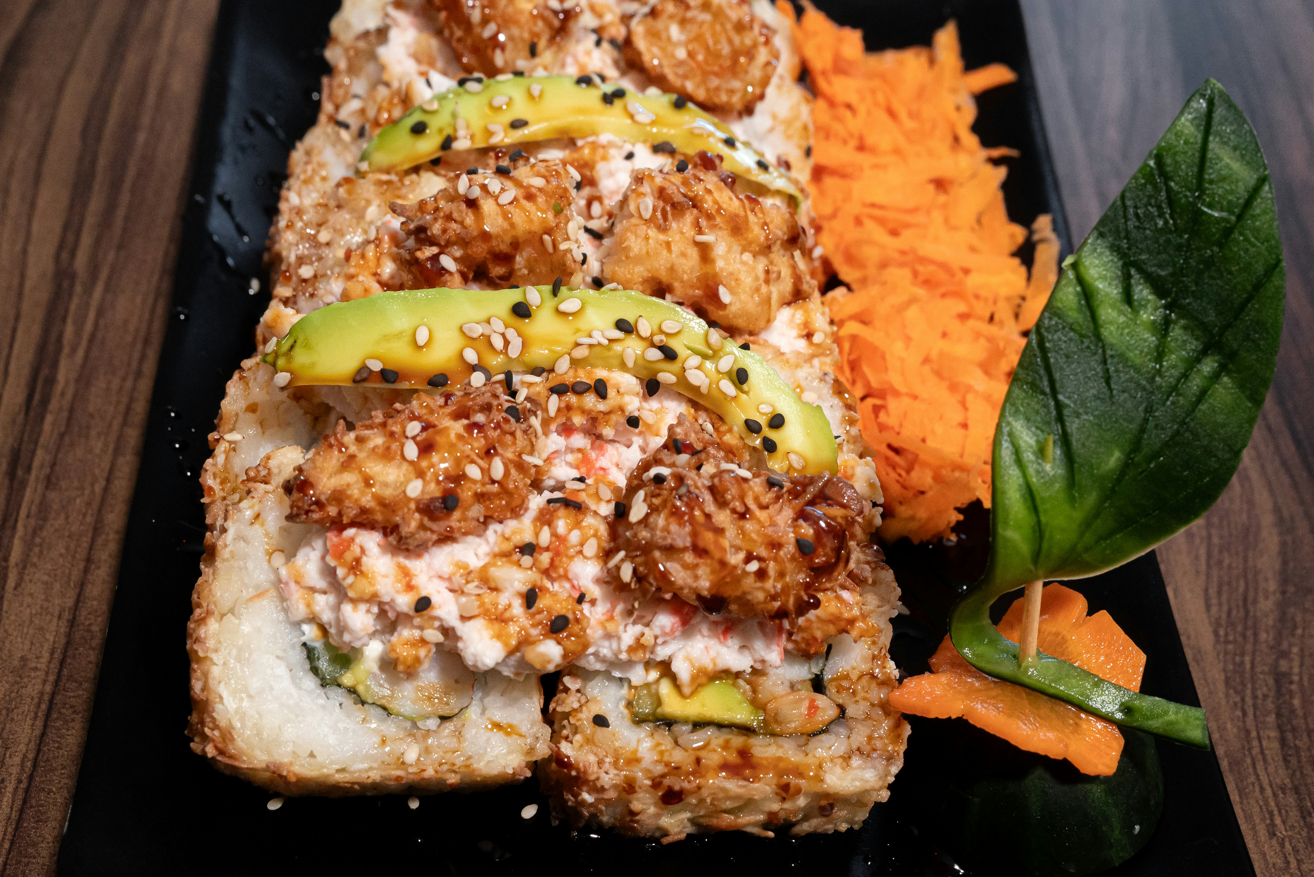 Crunchy topped sushi roll with avocado on a black plate
