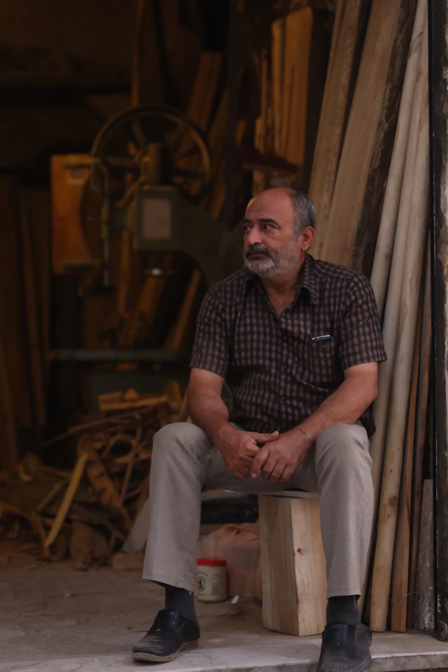 An older man sitting on a bench in a cluttered woodshop