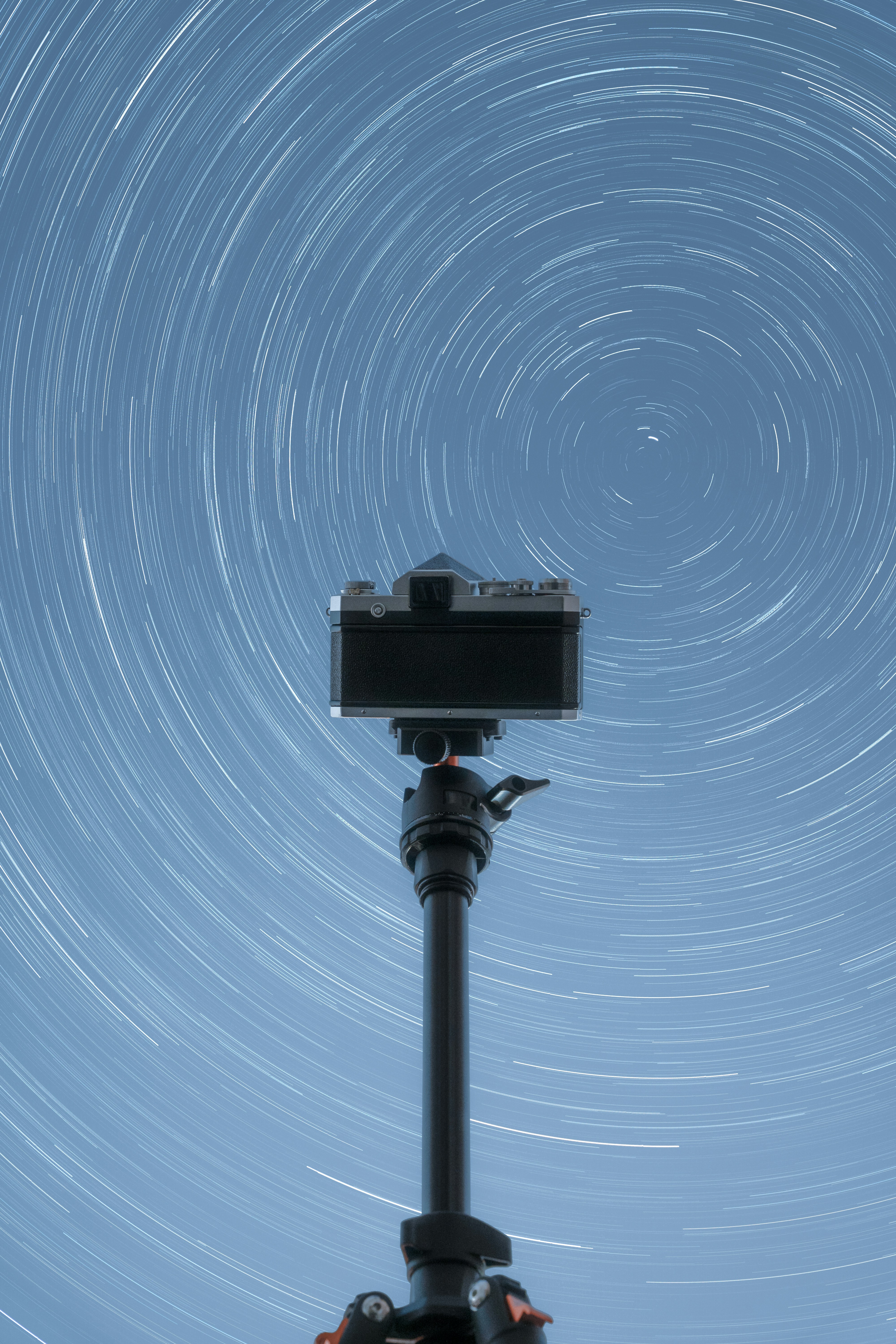 A camera on a tripod with a star trail in the background