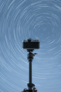 A camera on a tripod with a star trail in the background
