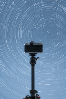 A camera on a tripod with a star trail in the background