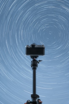 A camera on a tripod with a star trail in the background