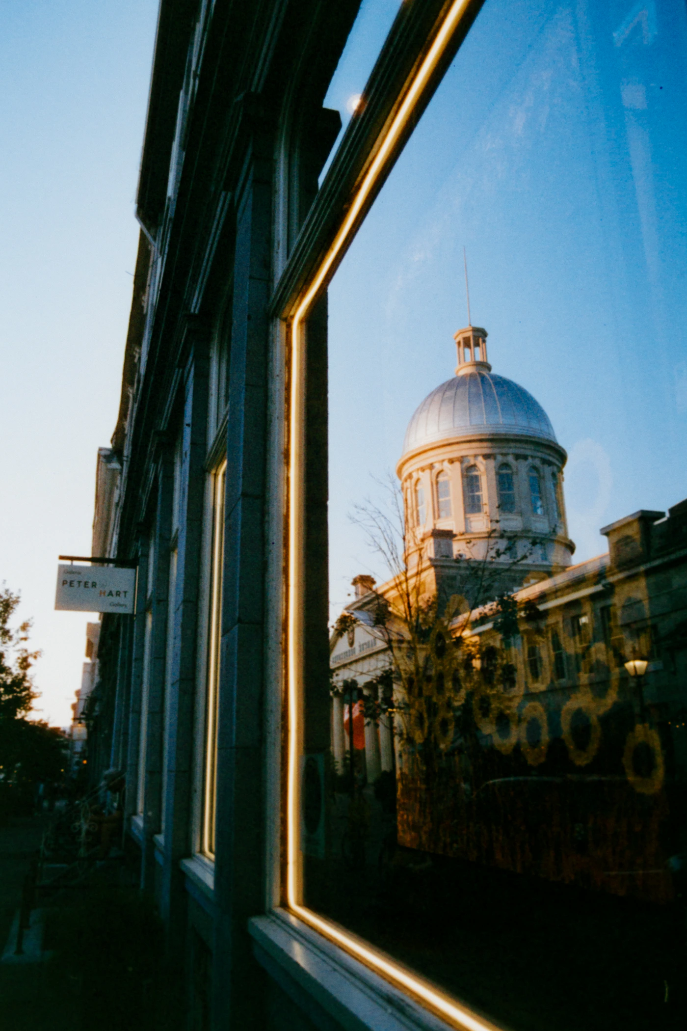 The Bonsecours Market silver dome in Old Montreal viewed through a heritage building window at golden hour, warm evening light catching the neoclassical dome
