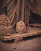 A couple of clay faces sitting on top of a piece of wood