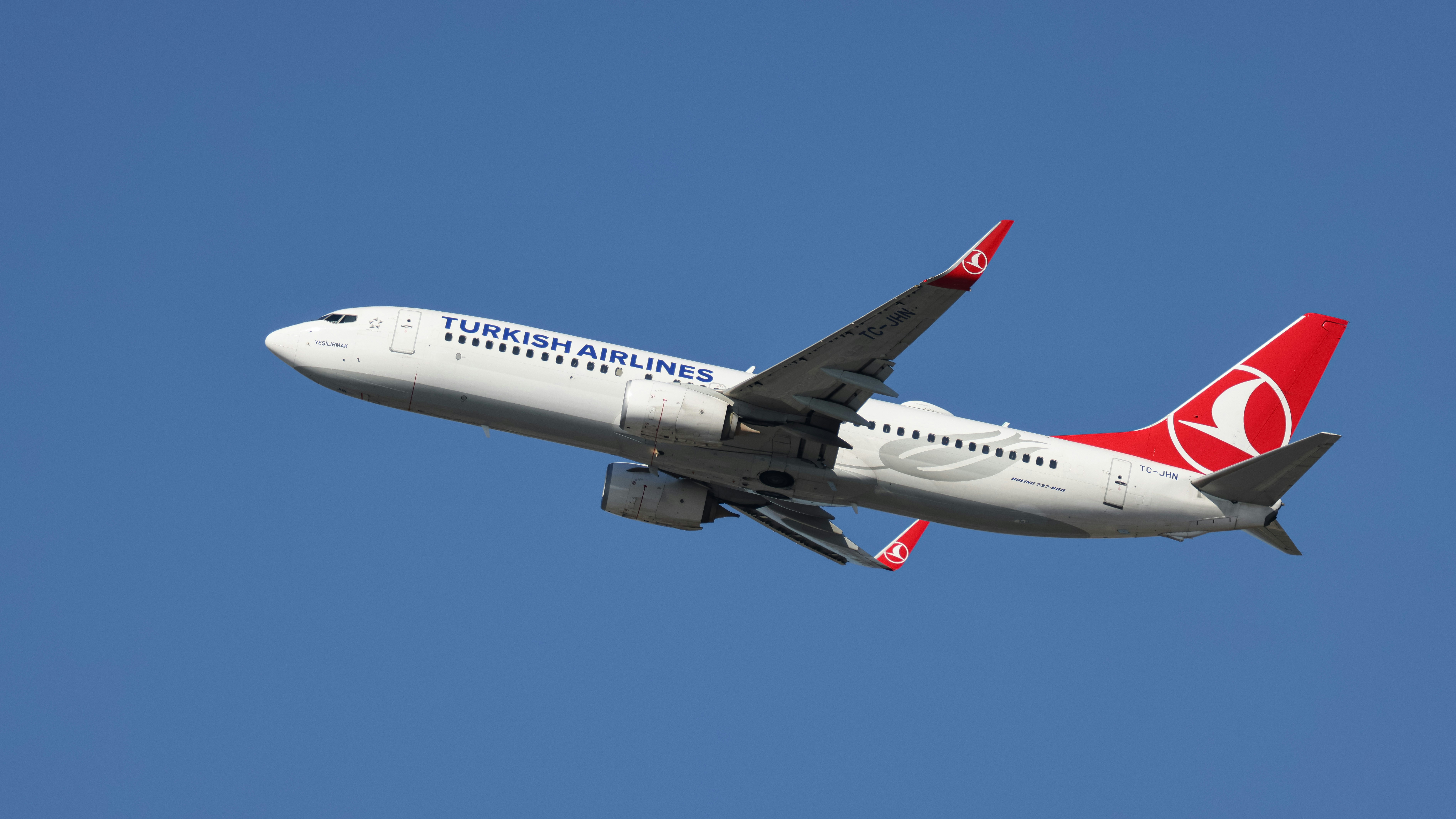 A large jetliner flying through a blue sky, A Turkish Airlines Boeing 737 soaring against a clear blue sky. Captured mid-flight, this image showcases the iconic red and white livery of Turkey