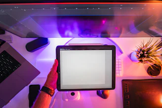 A person holding a tablet in front of a computer screen