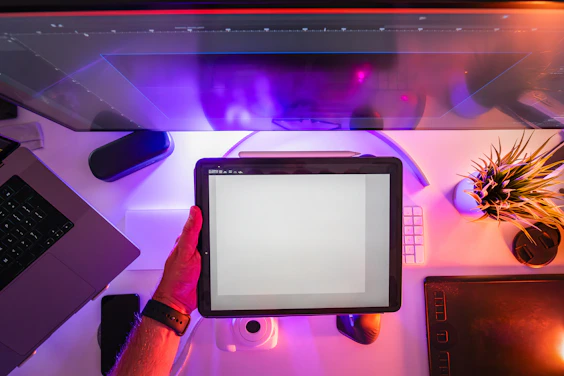 A person holding a tablet in front of a computer screen
