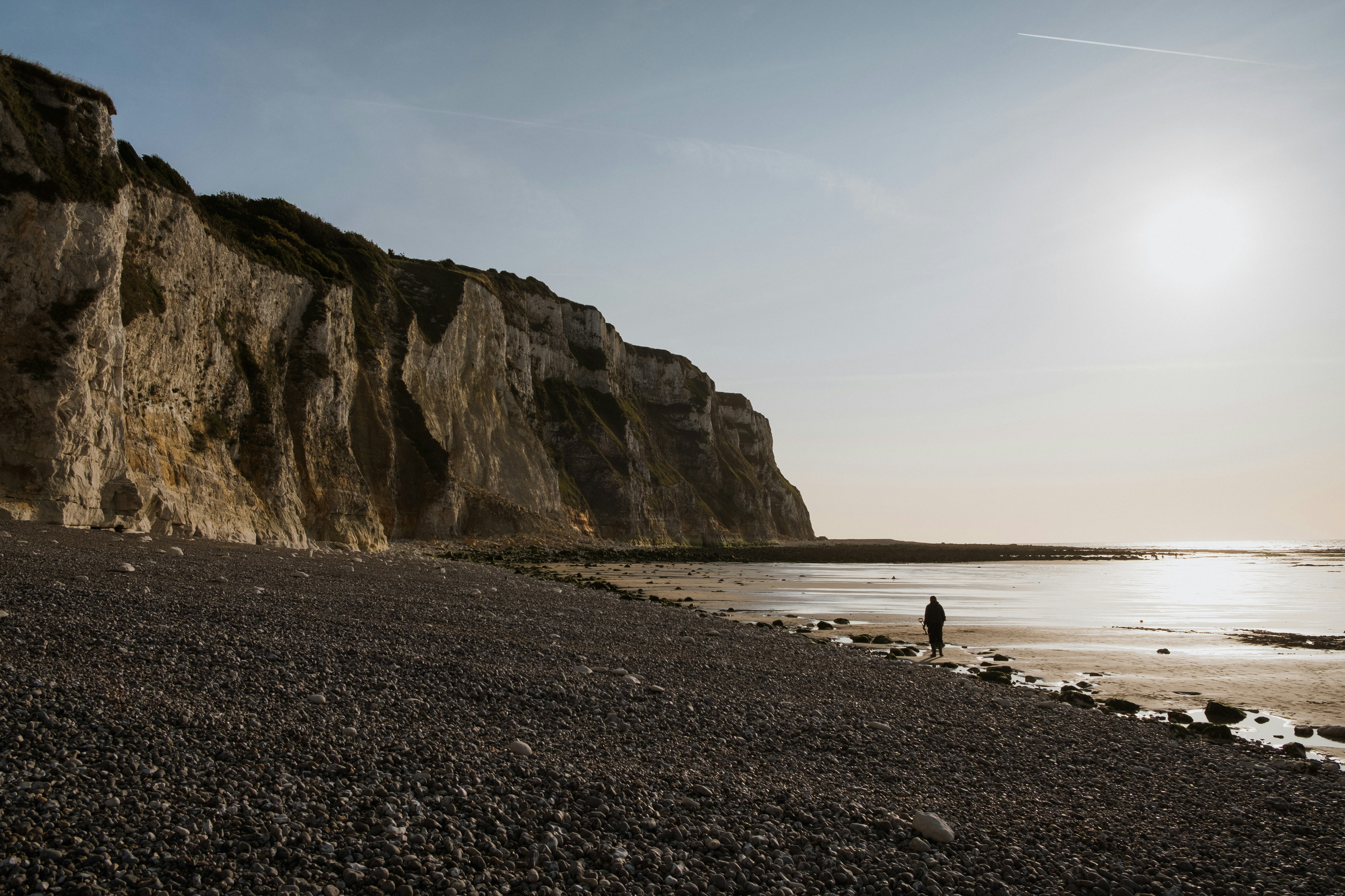 A person standing on a beach next to a cliff