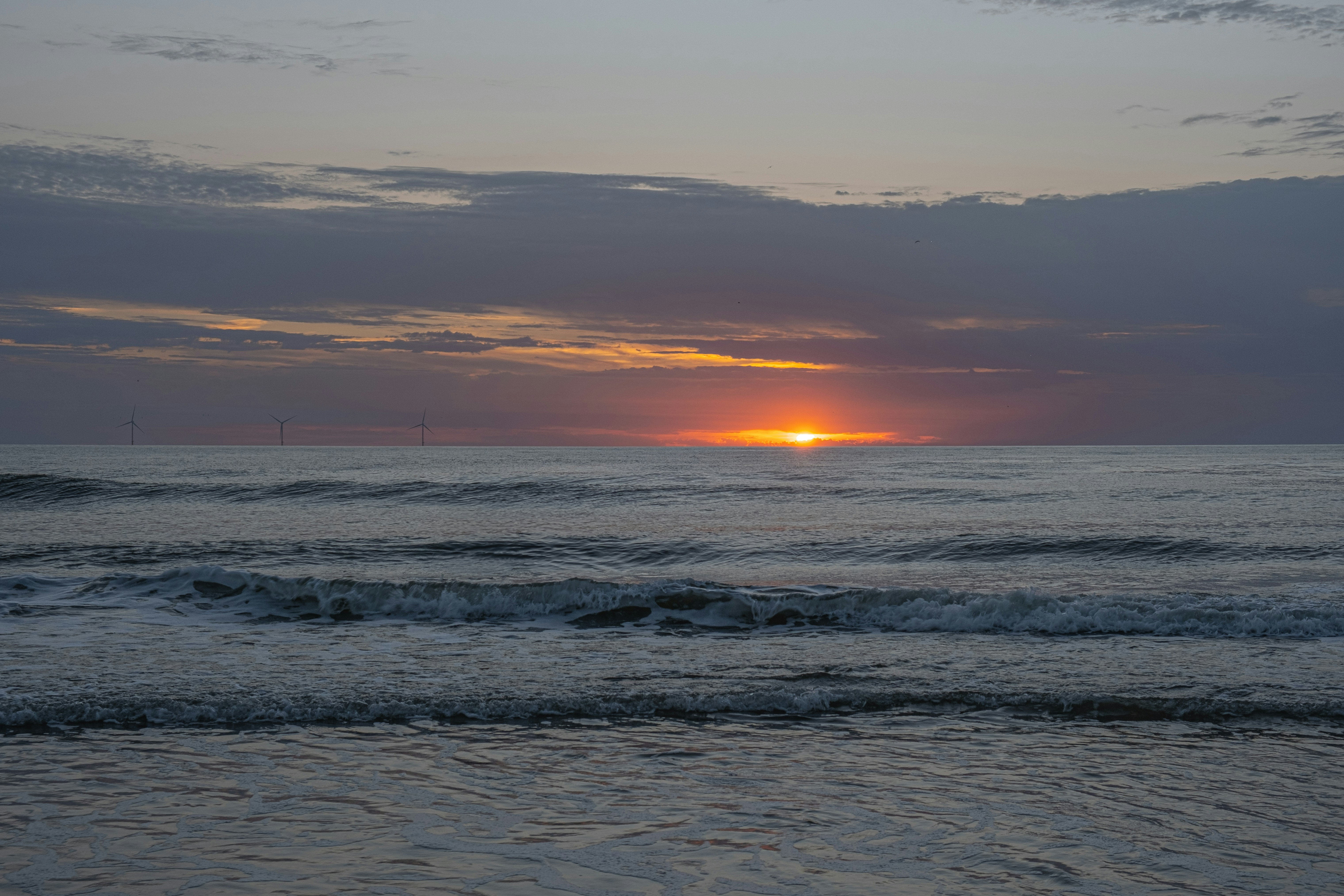 The sun is setting over the ocean on a cloudy day, 