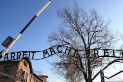 A large metal sign that reads arbet machere in front of a tree