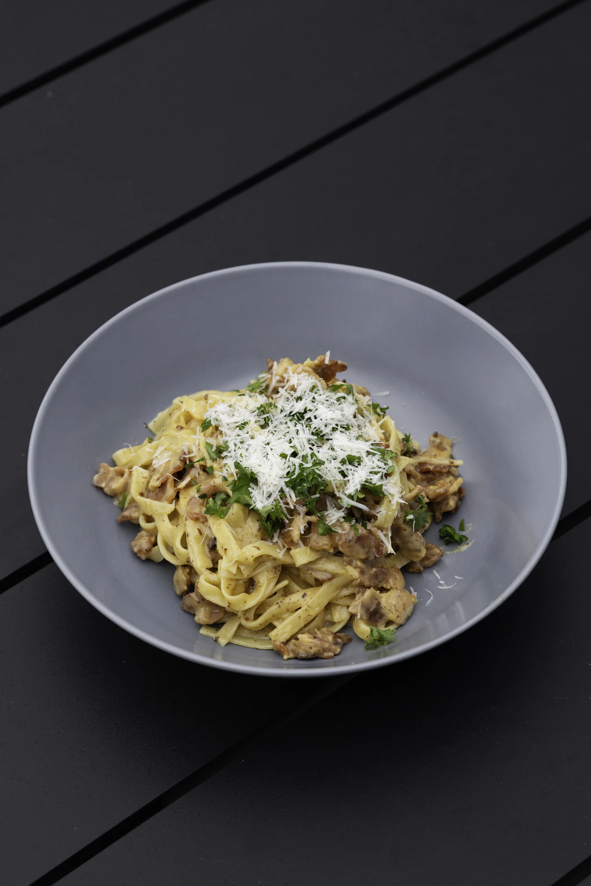 A plate of ribbon pasta under ragù and shaved Parmigiano, shot close on dark wood