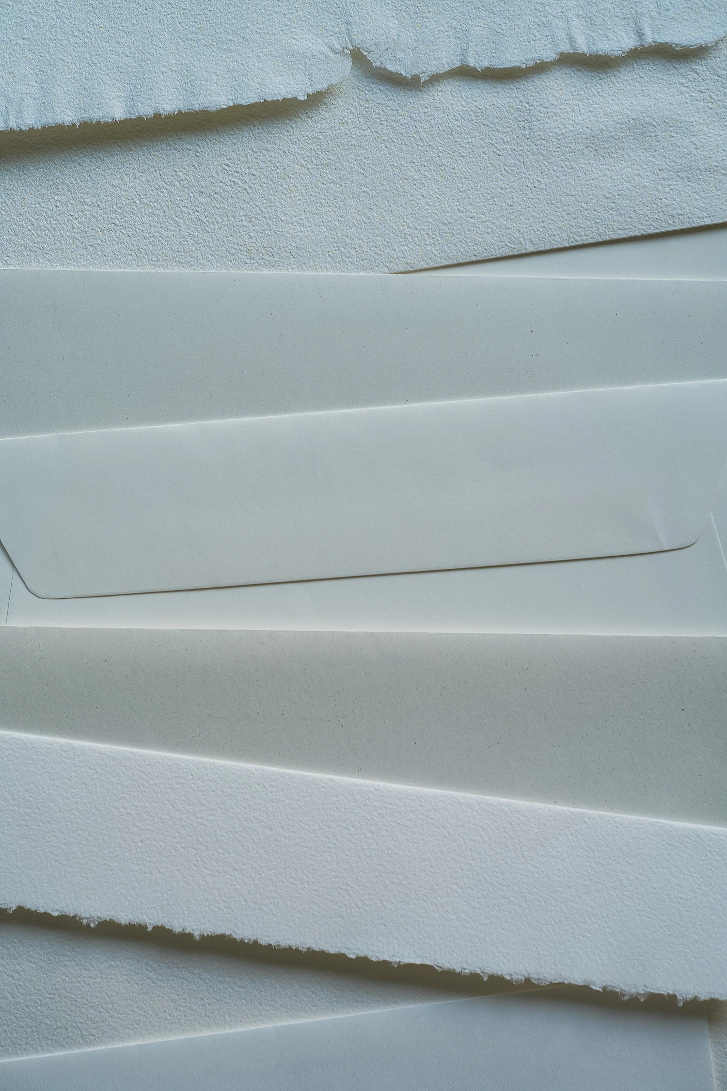 Sheets of white paper with torn deckle edges, layered one on another