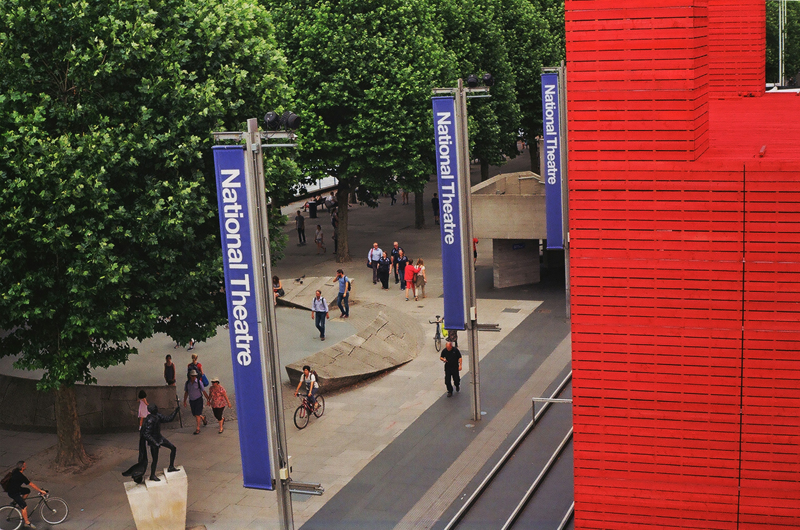 A group of people walking down a street next to a tall red building
