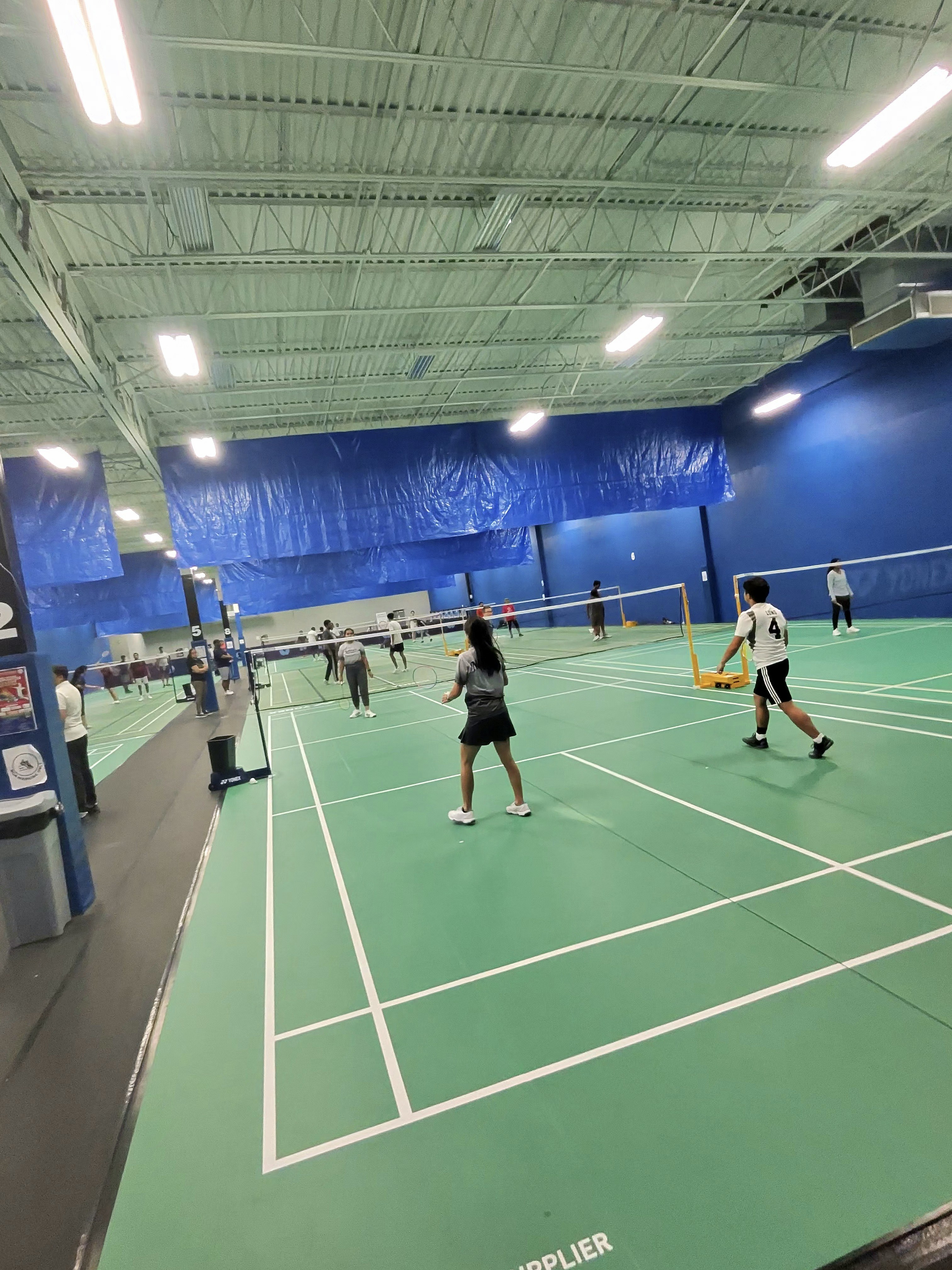 Indoor badminton court with wooden parquet flooring and white boundary lines
