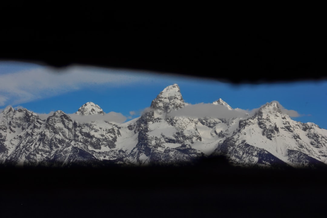 A view of a mountain range through a window, The view of the Grand Tetons from inside of a "Shane Cabin," a run-down cabin near Kelly Warm Springs and Gros Ventre in Grand Teton National Park, May, 2024. Its official name is the Luther Taylor Homestead.