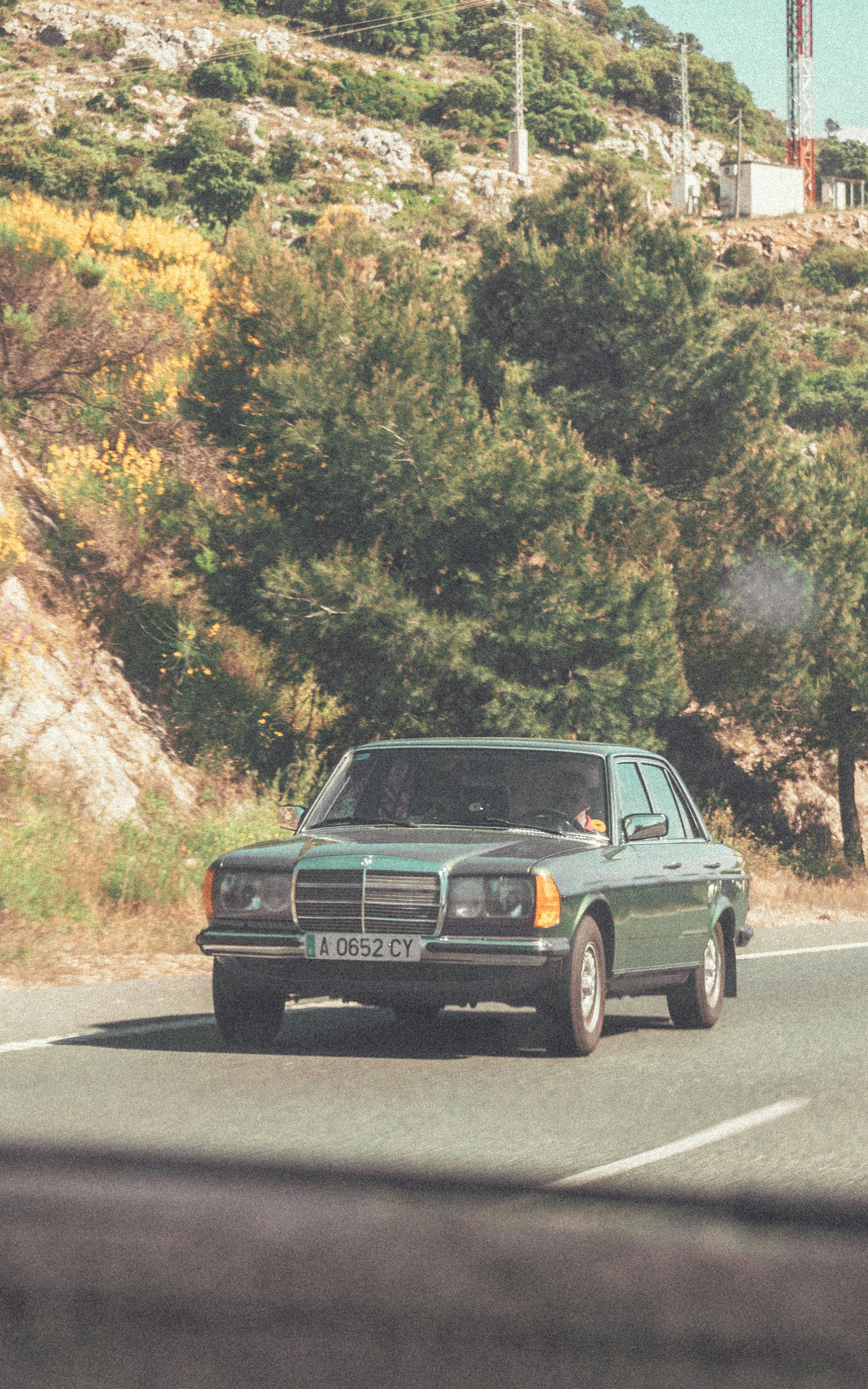 A green car driving down a road next to a hill