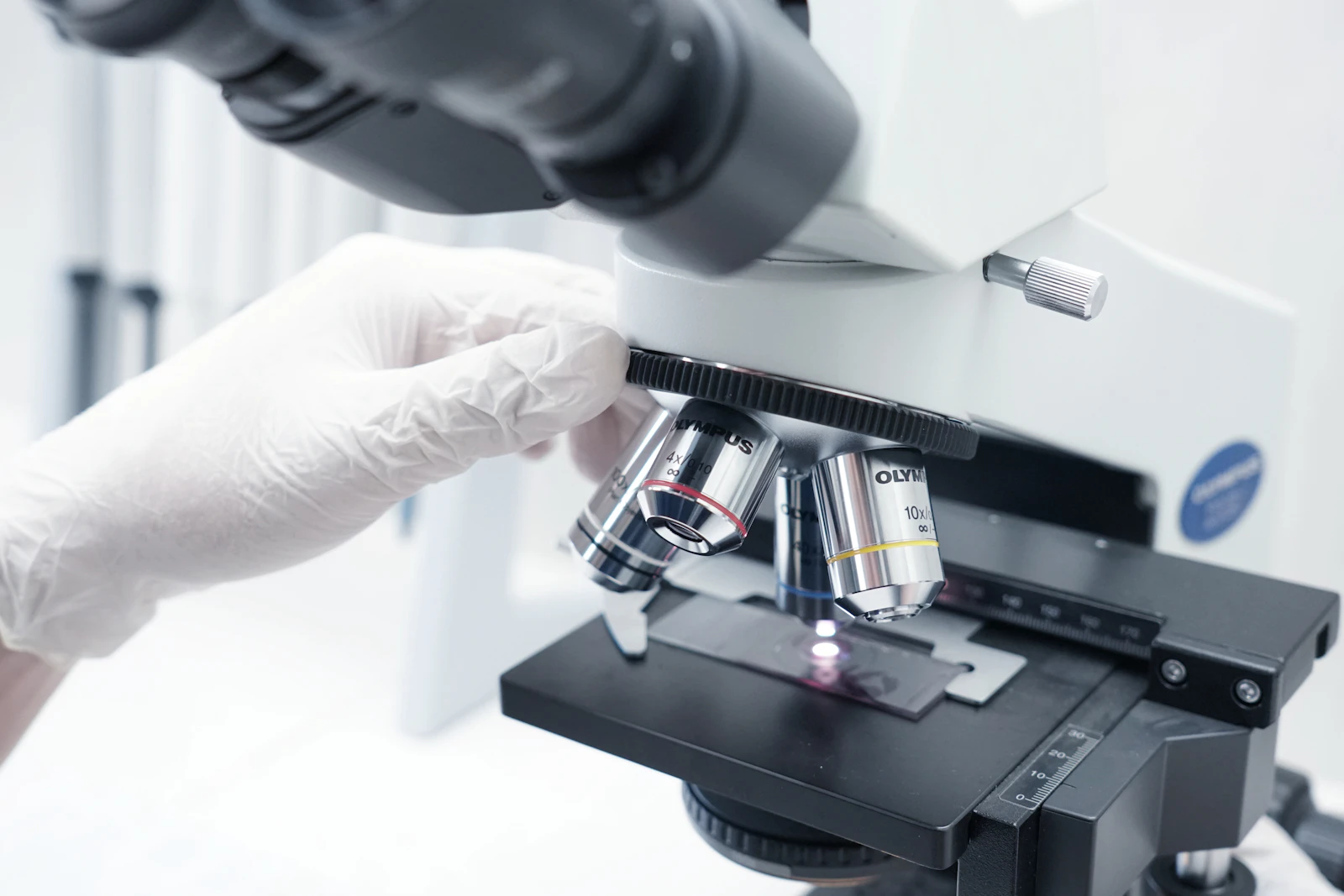 Technician in white gloves looking through a laboratory microscope