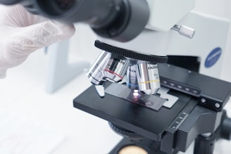 A person in white gloves is looking through a microscope